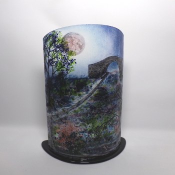Curved glass sculpture on black glass base. Stone canal bridge at full moon.