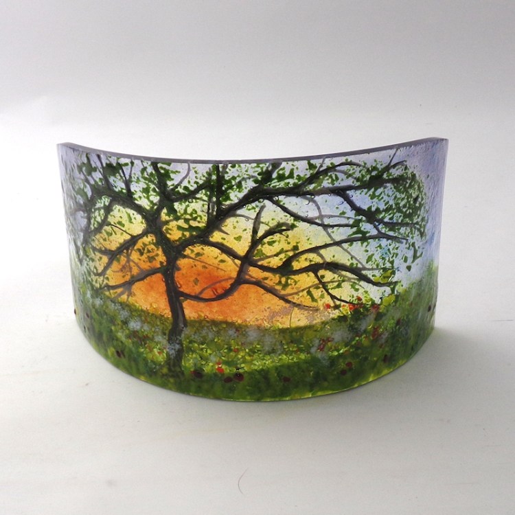 Curved glass freestanding sculpture featuring a tree at sunset with cow parsley in the foreground.