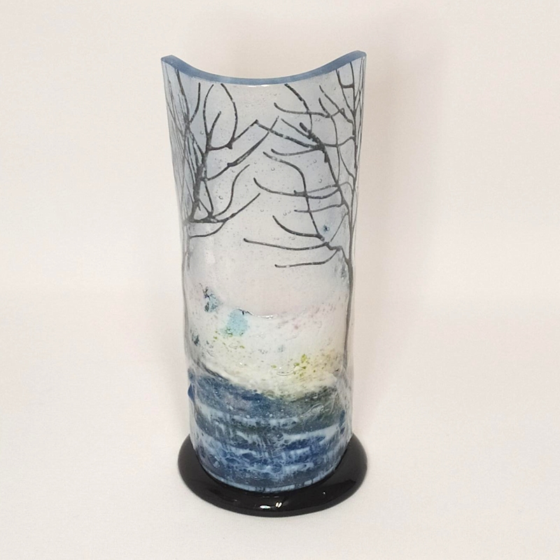 Small curved glass votive style sculpture showing two trees with snow and a frozen canal.