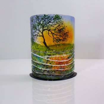 Curved glass sculpture on a black glass base. A tree with the sun setting below reflected in water. The water is represented by glass in sections.