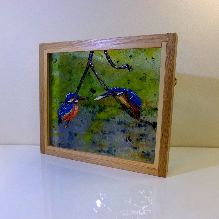 Fused glass picture of a young kingfisher being fed by a parent bird. Picture framed in oak.