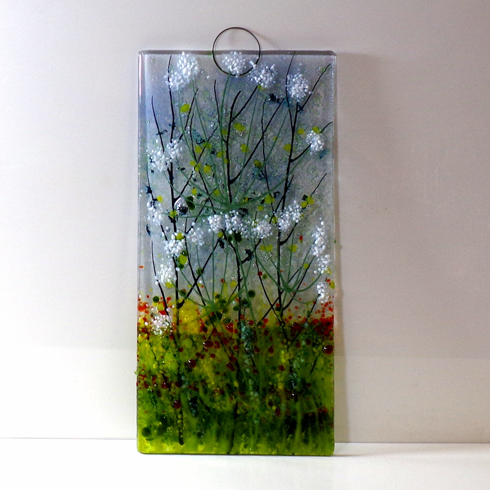 Large glass wall hanging with metal loops for fixings. A field of cow parsley with the red of poppies.