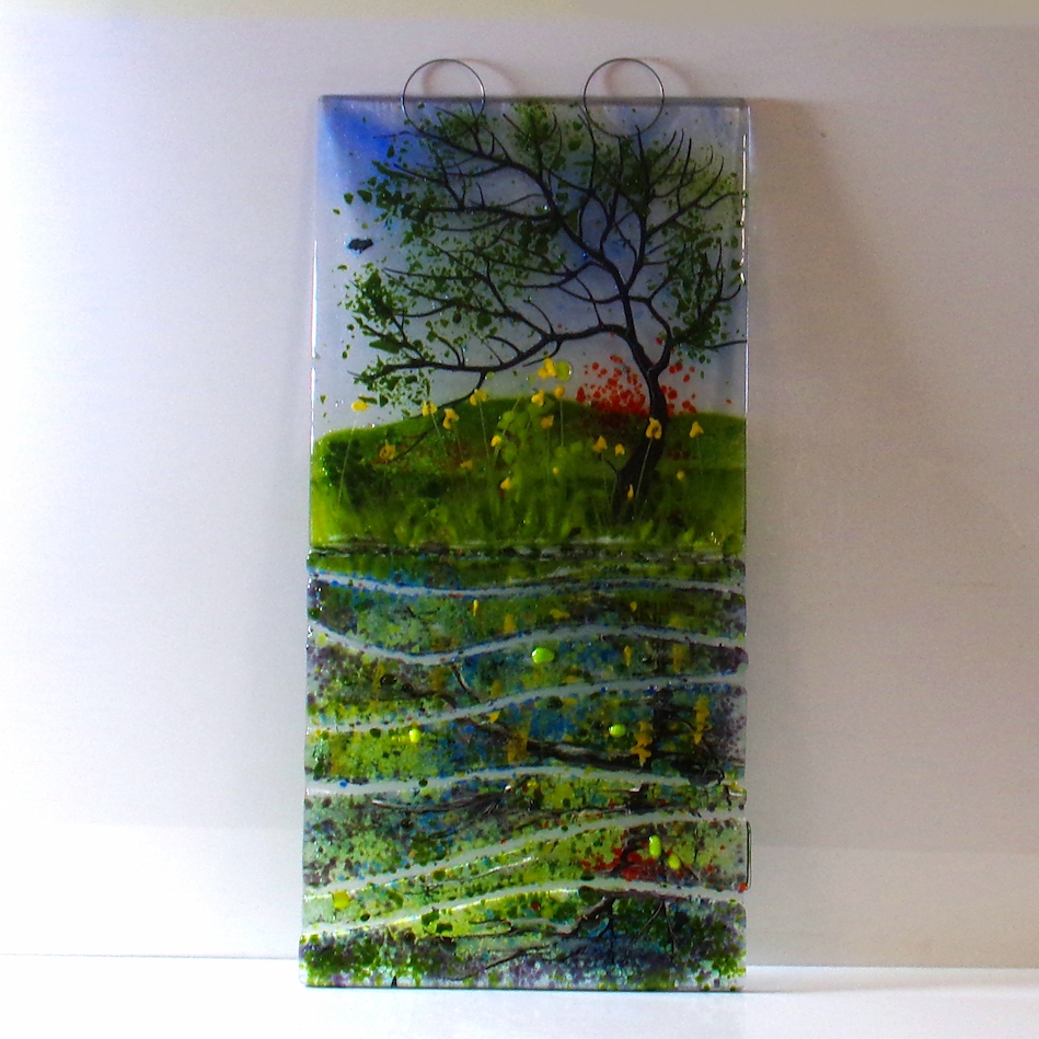 Large glass wall hanging with metal loops for fixings. Tree with Spring flowers, reflected in canal with the water being represented by sections of glass.
