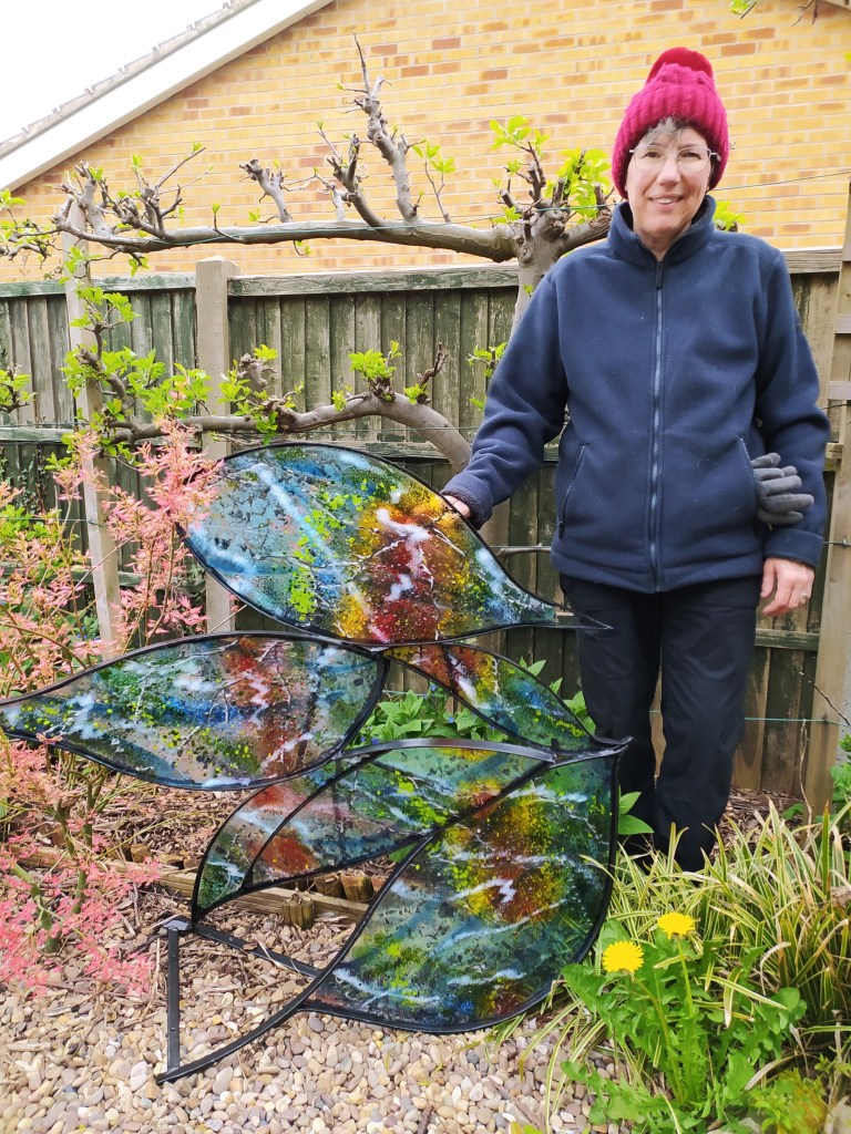 Coloured fused glass in leaf shaped sections in mild steel frame. Photographed with artist Kathryn Webley.