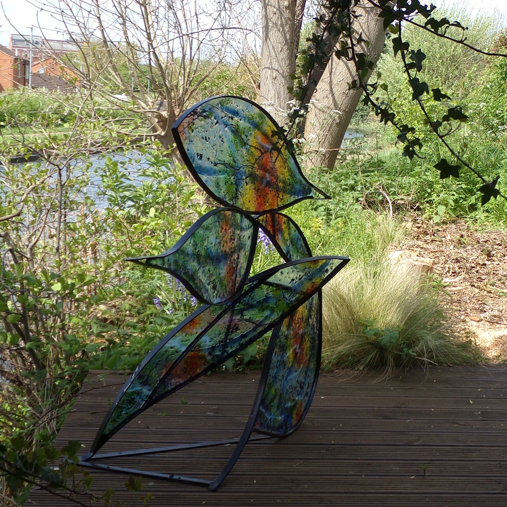 Coloured fused glass in leaf shaped sections in mild steel frame. Photographed near the canal.