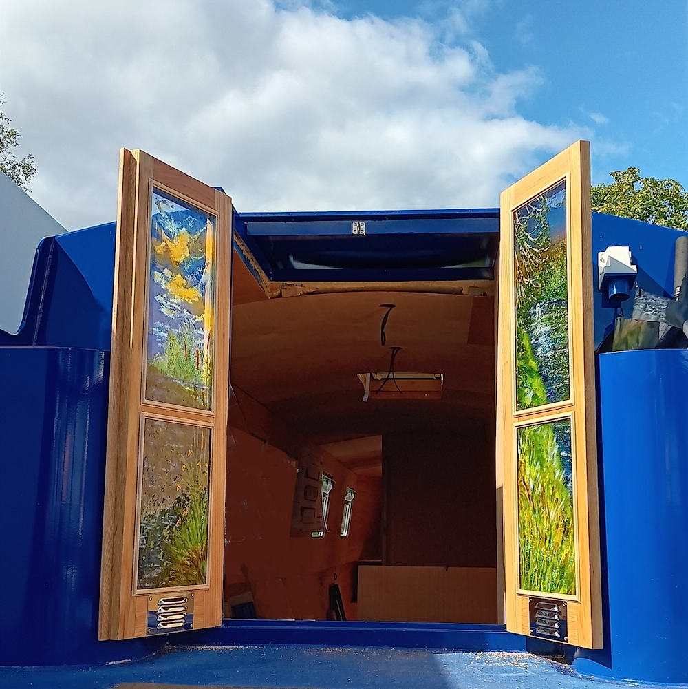 Stern doors open showing the design on the glass with the river bank and vibrant sky.