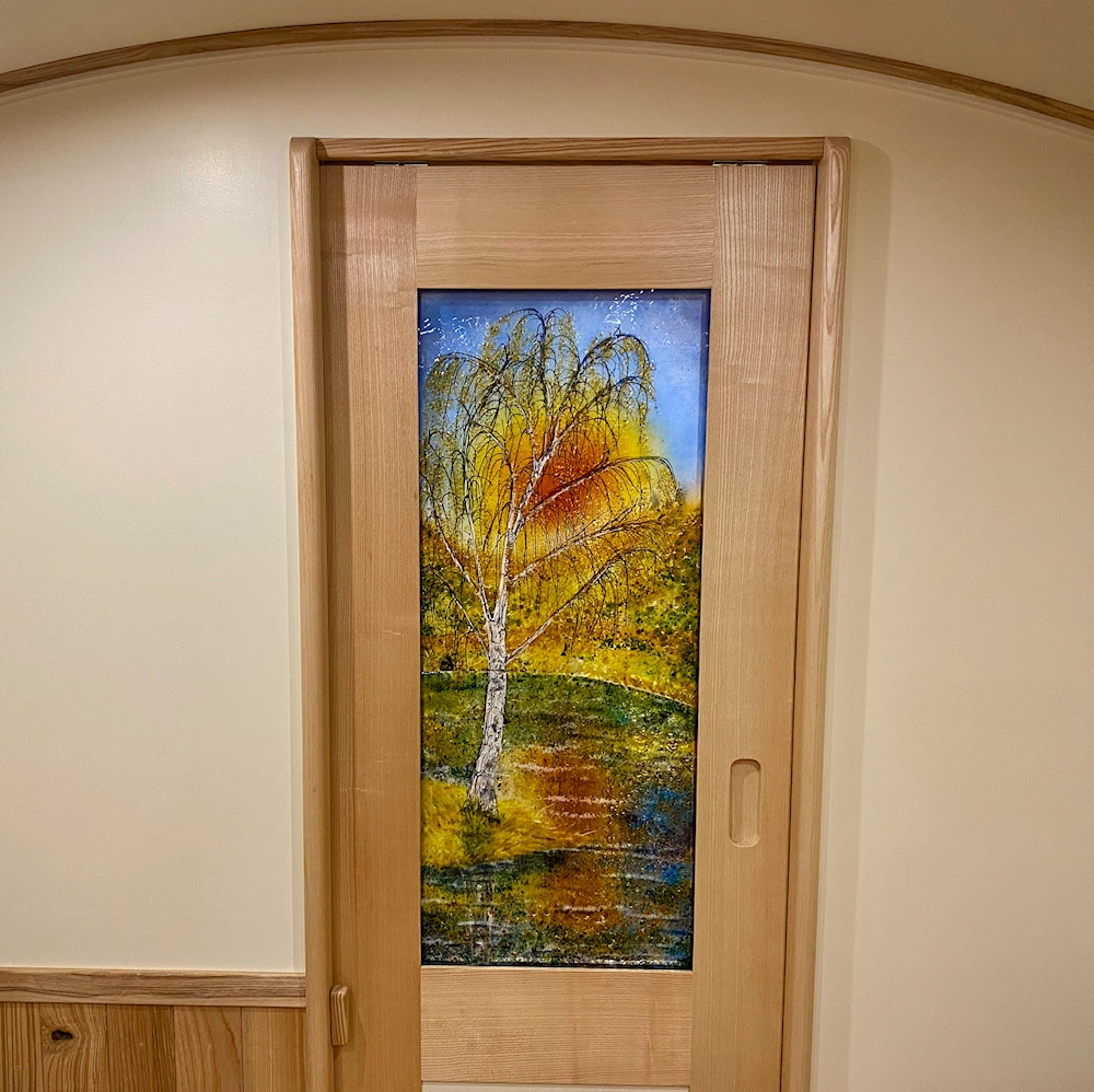 Fused glass interior door panel on a narrowboat. The design is a silver birth tree reflected in the canal at sunset.