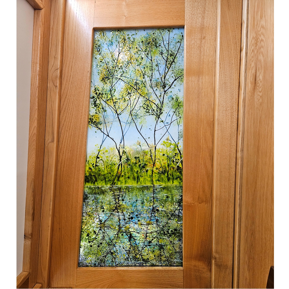 Fused glass door panel. Design is young trees reflected in the canal with Spring Flowers on the towpath.