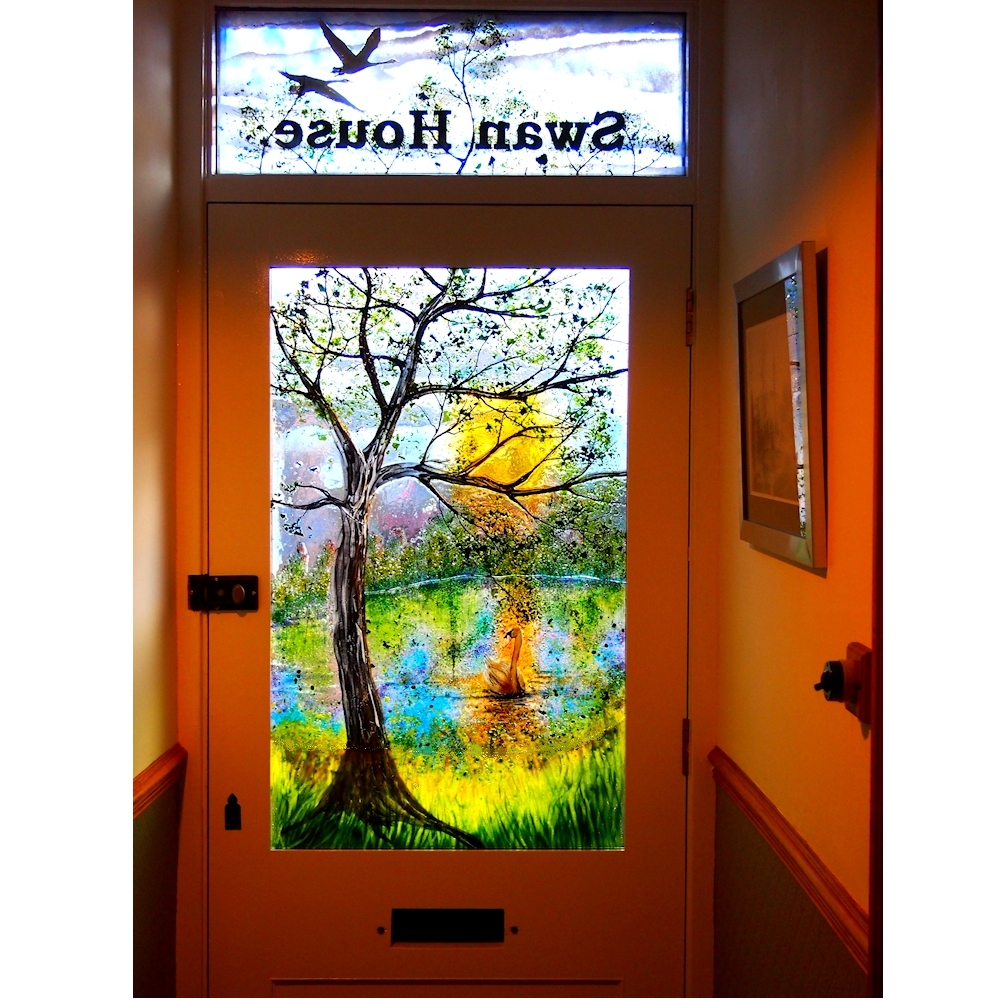 The completed door panels installed in the customers' home. View from the inside in daylight, showing the top panel with the name Swan House and the bottom panel with a single swan on the canal.