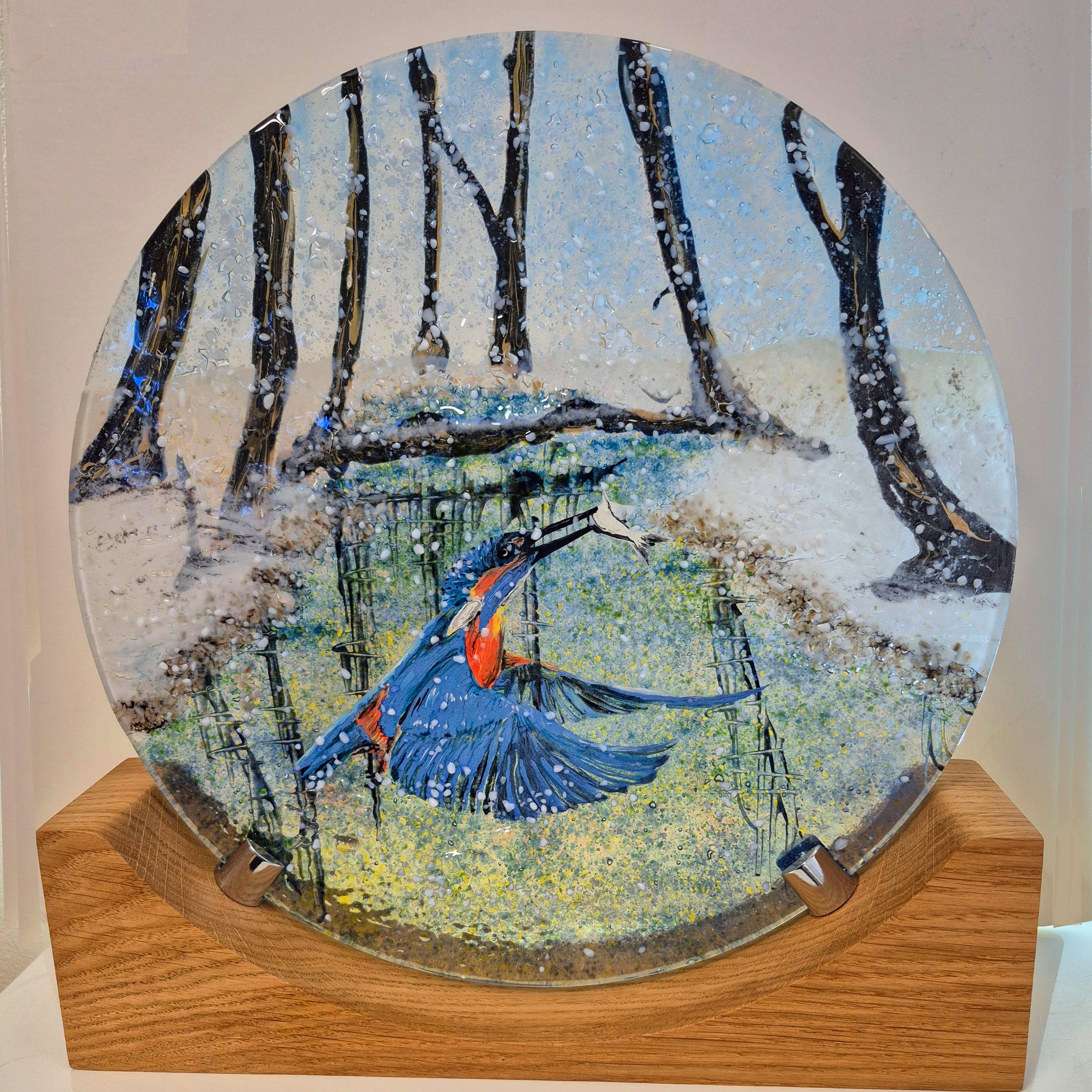 Fused glass disc mounted on a wooden base. The design is a kingfisher catching a fish from the canal. It is a snowy woodland setting.