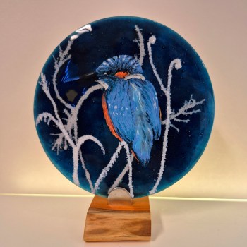 Fused glass disc mounted on a wooden base. The design is a Kingfisher perched on frost covered branches at nighttime.