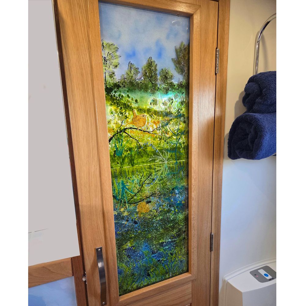 Glass door panel of a Spring canal scene with a Wren perched on a branch reflected in the water.