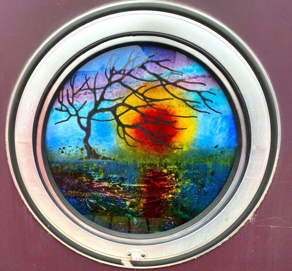 Porthole glass with a tree and sunset reflected in wate