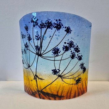 Curved glass sculpture featuring cow parsley against a twilght sky.