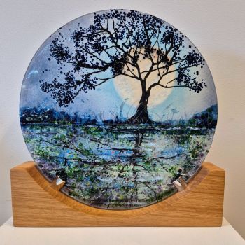 A disc sculpture on an oak stand. The design is a tree reflected in the canal with the moon rising in the background.