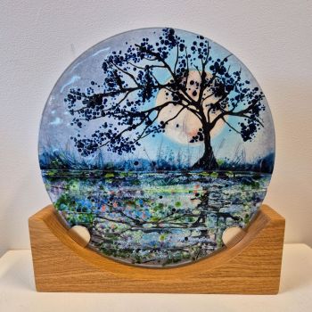 A disc sculpture on an oak stand. The design is a tree reflected in the canal with the moon rising in the background.