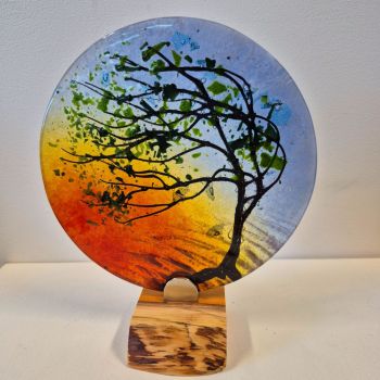 Glass disc sculpture on an oak stand, featuring a tree in Summer with the sky at sunset.
