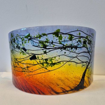 Curved glass sculpture of a tree in Summer with the sky at sunset.