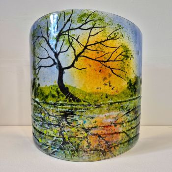 Fused curved fused glass sculpture. A Spring scene with a tree in the foreground with the sun setting behind. The scene is reflected in the canal with textured glass representing patterns in the water.