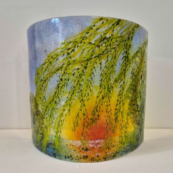 Curved fused glass sculpture with the branches of a Willow tree in the foreground; with the sun setting through the leaves.