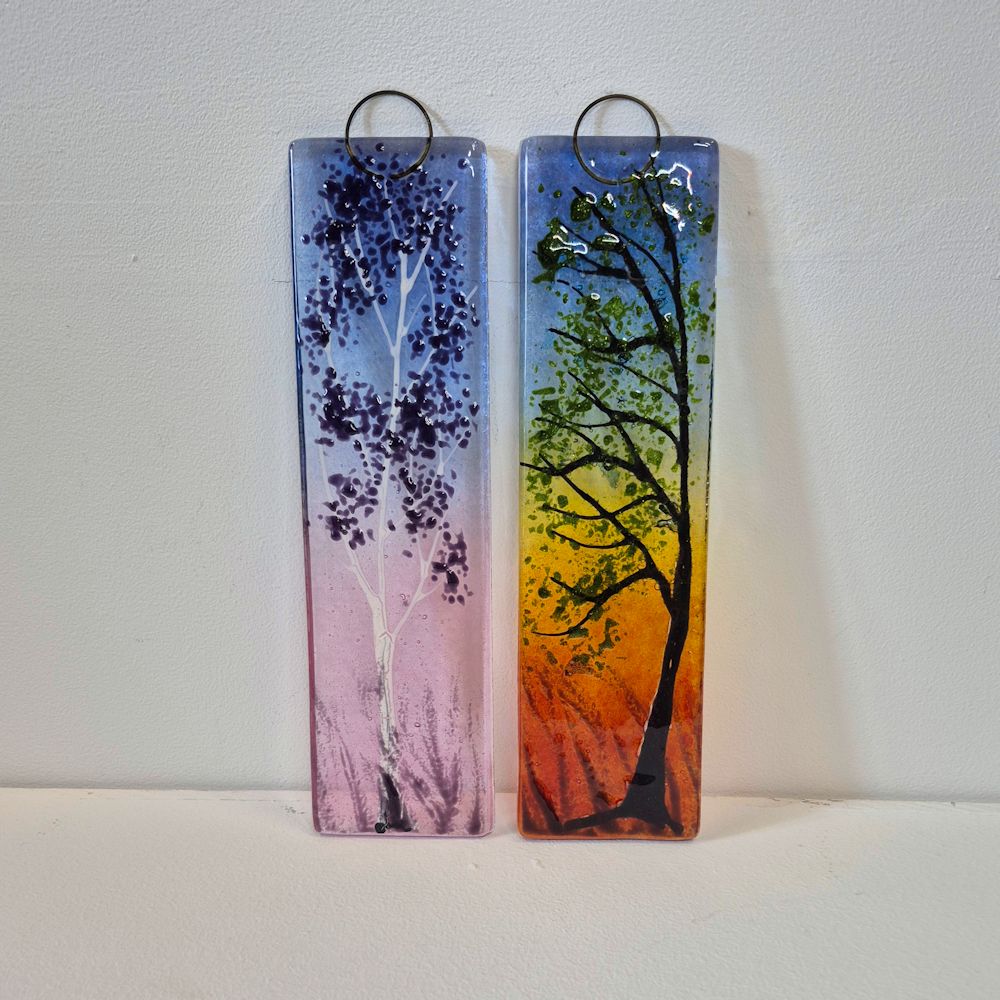 Two small fused glass wall hangings in designs inspired by the end of a day. Dusk is a Silver Birch tree with pink/purple colours. Sunset has a tree in the foreground with reds and yellows in the background.